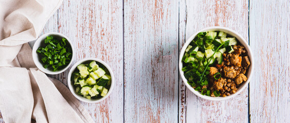 A bowl of buckwheat, meat, cucumber and green onions on the table top view web banner