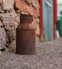 Rusty metal milk can against stone wall.