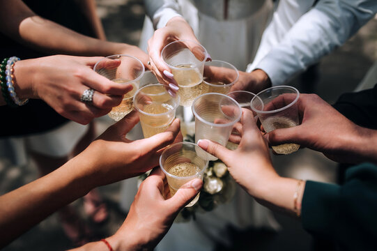Many people at a party, wedding, celebration hold plastic glasses of champagne in their hands.