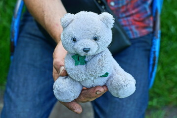 one white dirty beautiful soft with black eyes and nose small funny gift children's plush toy bear in hand of man daytime outdoors