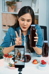 Smiling young beautiful Asian reviewing tasty mixed strawberry and cherry juice detox drinks,...