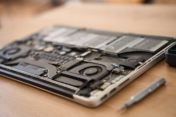 This is a closeup view of a disassembled laptop along with various repair tools arranged on a wooden table