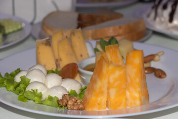 A plate of cheese and bread, with one slice of orange cheddar cheese, mozzarella balls, salad leaves, and walnuts on the side