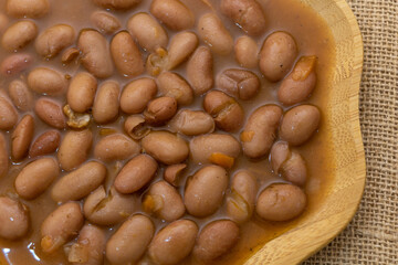Boiled beans in brown sauce, top view, on a wooden plate, close-up, on a burlap background
