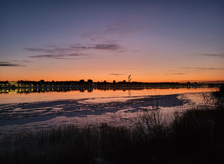 Obraz premium The outline of the city against the background of a pink sunset over a winter river
