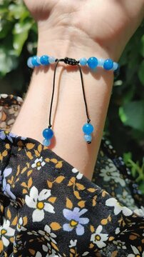 Blue stones kyanite aquamarine apatite beaded bracelet on woman's wrist. Green leaves background, sun rays and shadows, summer. Semiprecious stone shamballa macrame chakra bracelet, jewelry, accessory