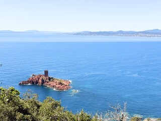 Scenic view of &Icirc;le d'Or, a small rocky island with a medieval-style tower in the Mediterranean Sea off the coast of Saint-Rapha&euml;l, France, with blue water and distant coastline under a clear sky.
