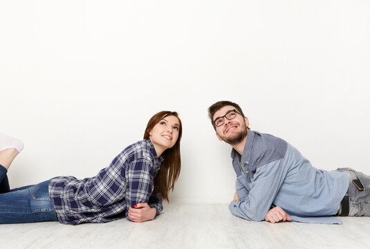 Dreamy couple lying on floor in empty room and looking up, imagine future interior design project, white background