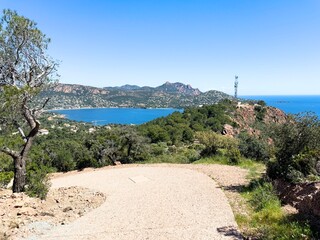 Scenic view of the Esterel mountains and the coastline near Saint-Rapha&euml;l in southern France, with a gravel path in the foreground, lush greenery, and the deep blue Mediterranean Sea under a clear sky
