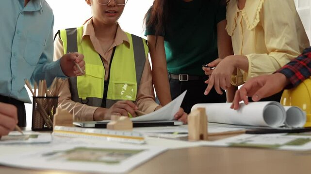 Smart architect and safety engineer discussion about building blueprint on table with architectural document, measurement tools and wooden block scatter around at modern office. Closeup. Delineation.