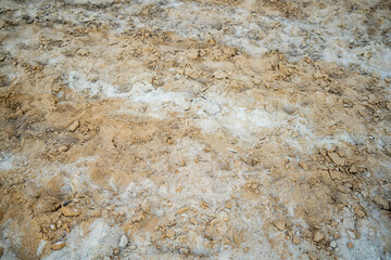 A close-up shot of textured sand, mixed with some small rocks and lighter material, fills the frame. The focus is on the details of the sands surface.