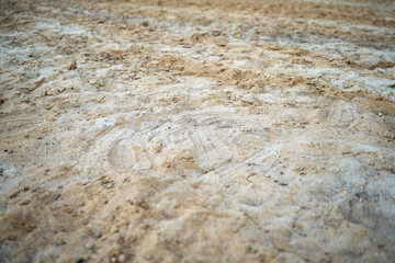 A close-up shot of textured sand, mixed with some small rocks and lighter material, fills the frame. The focus is on the details of the sands surface.