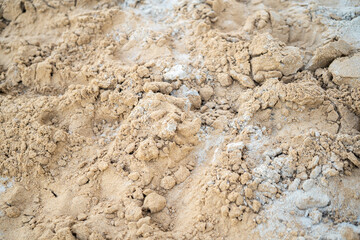 A close-up shot of textured sand, mixed with some small rocks and lighter material, fills the frame. The focus is on the details of the sands surface.