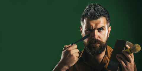 Barbershop accessories. Barber man with straight razor, wooden box and shaving brush. Beard care. Serious bearded guy with vintage razor for shaving. Barbershop advertising. Banner design. Copy space.