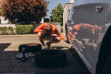 Man changing car tire on roadside using tools, vehicle lifted on jack. Concept of auto repair,...