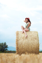 Woman on hay bale with upward gaze and confident posture in rural setting