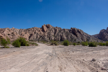 Dirt road in the desert named Quebrada de las Flechas with mountains of sedimentary rocks in Salta Province, Argentina