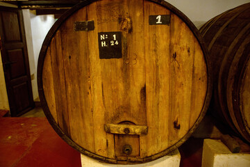 Rows of traditional oak wine barrels carefully stacked in a dimly lit winery cellar, aging fine wine to perfection