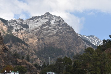 Snow-capped mountains with green trees under a bright sky near Nainital.