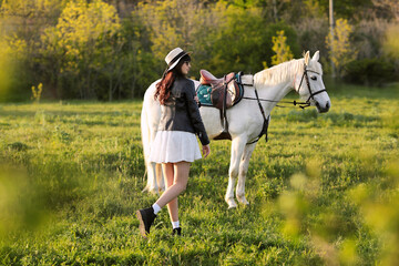 Beautiful young girl with dark hair on a white horse in a field at sunset in spring