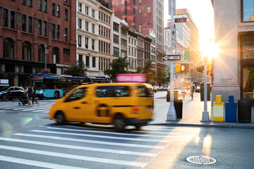 Busy intersection with people, taxis and buses on 5th Avenue and 23rd Street in New York City with sunlight shining in the background