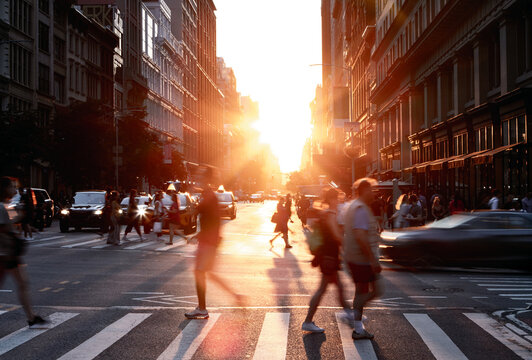 Busy intersection with people and cars in motion on 5th Avenue and 23rd Street in New York City with sunlight background