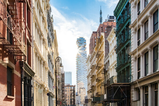 Old historic buildings contrast against a modern glass skyscraper on Greene Street in the SoHo neighborhood of New York City