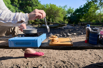 Unrecognizable person toasting slices of bread on a portable gas stove for breakfast outdoors at a campsite.