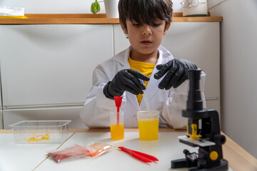 Young boy doing science experiment with yellow liquid and microscope