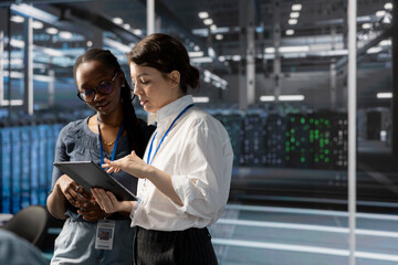 Engineers in data center using device, verifying firewall configurations. Teamworking IT professionals performing equipment vulnerability scans in server hub using tablet