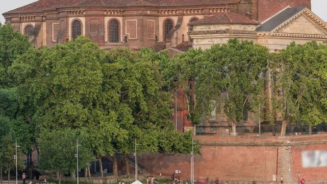 Aerial view of Port de la Daurade park along the Garonne River timelapse in Toulouse, France. Sunset orange light, ferry at the dock and people enjoying the vibrant riverside atmosphere