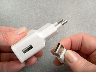 The woman's hands connect or disconnect the USB cable and AC power adapter. AC power charger with...