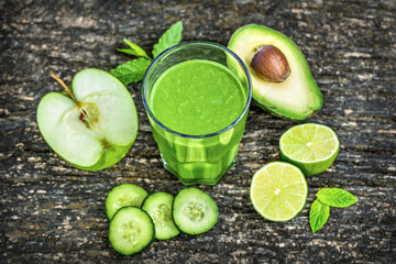Glass of green detox smoothie with avocado cucumber lime and apple on rustic wooden background, healthy detox drink concept