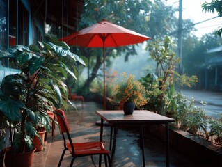Red umbrella protecting table, tropical plants, and flower on the side of house