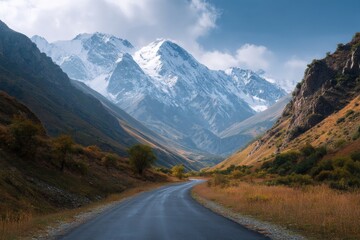 Winding road through alpine valley, snowy peaks in distance under blue sky.