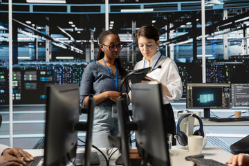 Team of technicians using tablet in server farm, analyzing data. Women working in data center...