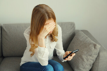 Sad upset crying woman holding phone suffering from stress after reading emotional message at home