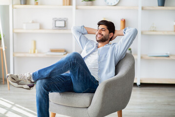 Lazy day. Relaxed arab man resting on comfortable armchair, holding hands behind head. Guy sitting with closed eyes and enjoying weekend in home interior