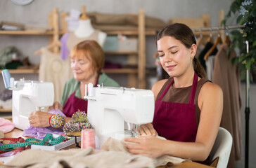 Experienced seamstress works in a team with an assistant, they sew clothes in the workshop. Dressmakers sew fabric on sewing machines