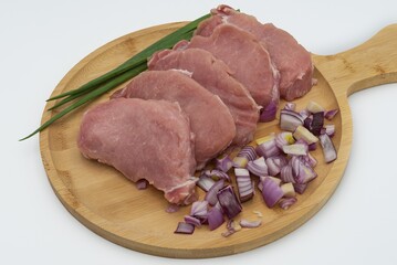 Raw pork steaks with sliced ​​red onion and green onion on wooden board ready to cook
