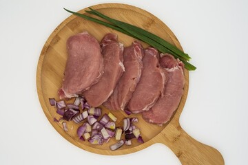 Raw pork steaks with sliced ​​red onion and green onion on wooden board ready to cook