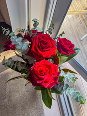 Dark red rose in a vase on a grey floor matt nearby window and wooden patio deck in New Zealand.