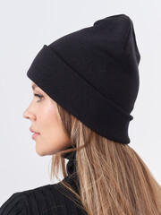 Side profile of a person wearing a black knitted beanie and black ribbed sweater, with long brown...