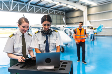 Female pilots using laptop and preparing flight plan in hangar