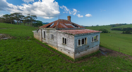 A decaying abandoned house with a rusty roof stands on a green rural hillside, a symbol of neglect...