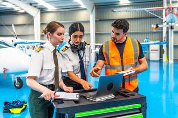 Aircraft maintenance engineer showing data on laptop to female pilots in hangar