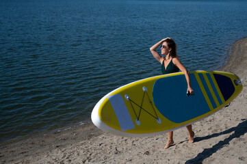Caucasian woman walks along the beach and carries a sup board on the river in the city. Summer...
