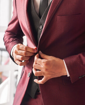 Manos novio abrochandose boton de traje boda colores calidos traje vinotinto