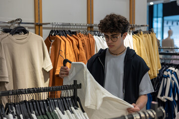 Teen boy choosing stylish t-shirt in clothing store. Young customer shopping trendy casual wear at...
