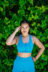 Young sportswoman pointing finger to her head in front of green leaves wall